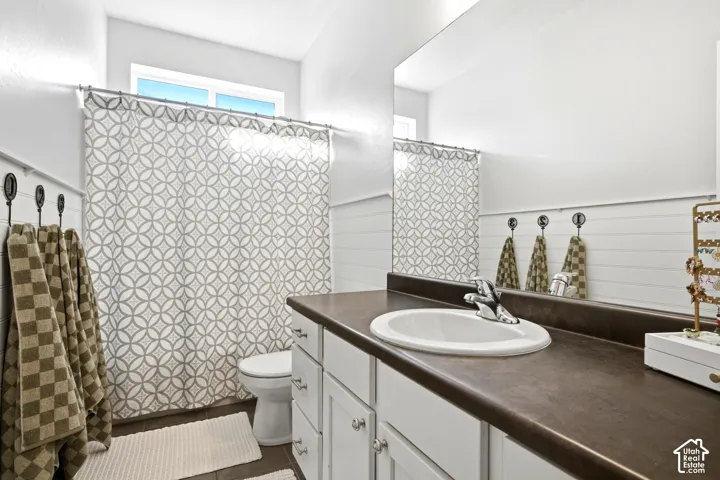 Bathroom featuring white cabinetry, solid-surface countertop with an integrated basin, shiplap wall detailing, and a wall-to-wall mirror