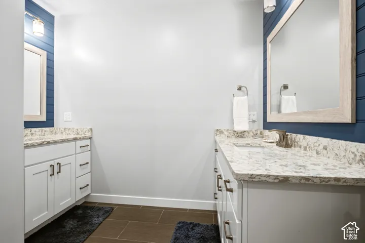 Dual white vanities featuring speckled stone countertops, brushed metal hardware, wall-mounted mirrors with light-wood frames, and deep blue horizontal shiplap accent walls
