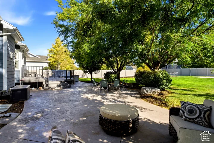 Stamped concrete patio featuring an elevated wood deck with metal railing, mature trees, and privacy fencing