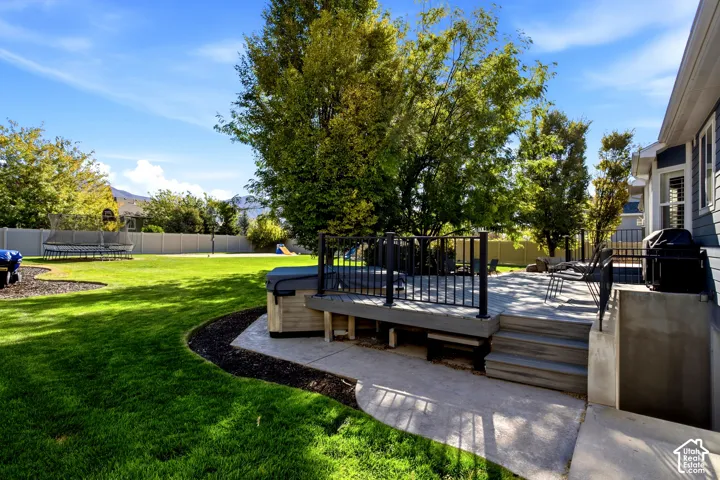 Expansive backyard featuring a composite deck with black metal railing, a built-in hot tub, concrete patio space, and mature trees