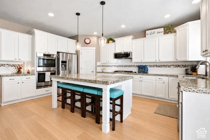 Kitchen featuring white shaker-style cabinetry, stone countertops, stainless steel double wall ovens, a central island with decorative legs, and wood-finish flooring