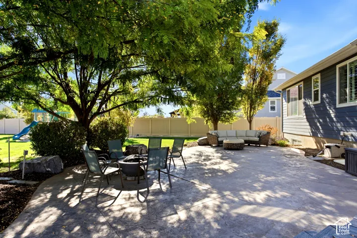 Stamped concrete patio featuring mature trees, landscaped stone borders, and vinyl privacy fencing