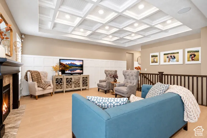 Coffered ceiling with recessed lighting, floor-to-ceiling wainscoting, fireplace with stone-finish surround, wood-finish flooring, and wooden stair railing