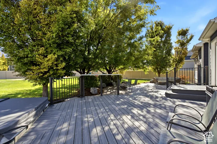 Multi-level composite deck featuring metal railing, a built-in spa, and mature trees overlooking a fenced yard