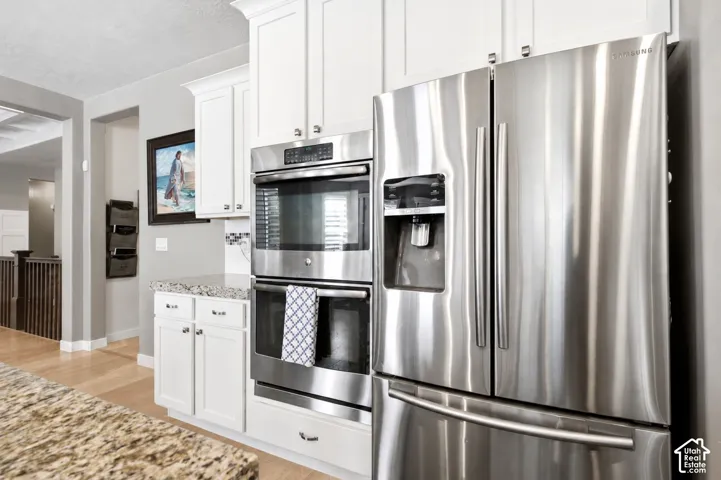 Kitchen featuring white shaker-style cabinetry, stainless steel double wall ovens, a stainless steel French-door refrigerator, and stone-finish countertops