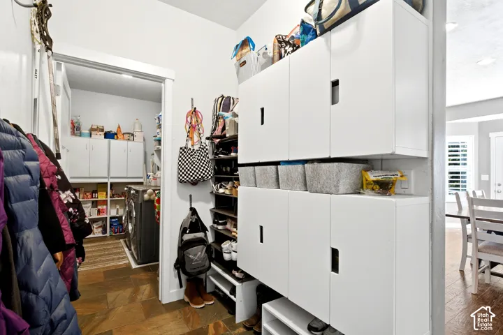 Utility area featuring stone-finish tile flooring, white wall-mounted storage cabinetry, and integrated shelving