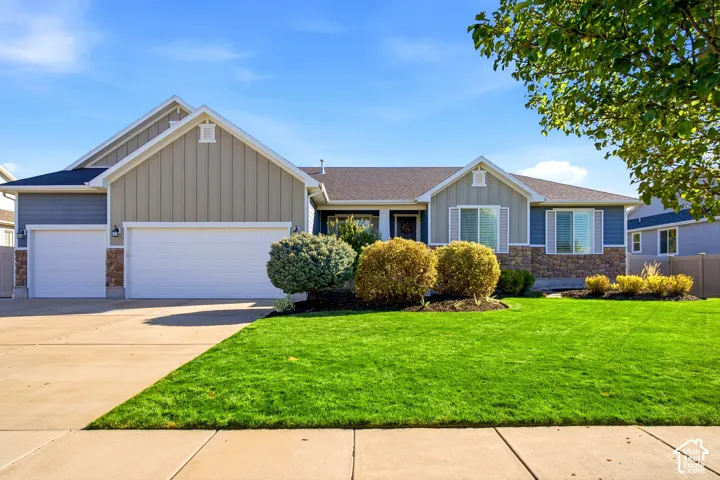 Single-level residence featuring a multi-textured exterior of vertical panel siding and stone veneer, a three-car garage, and a manicured front lawn