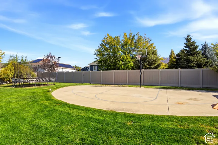 Backyard featuring a concrete basketball court with a hoop, a fenced perimeter, and a manicured lawn