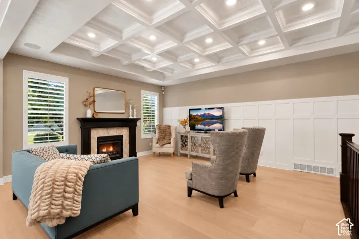 Coffered ceiling with recessed lighting, fireplace featuring a dark surround and stone-tiled hearth, board-and-batten wainscoting, wood-finish flooring, and plantation shutters