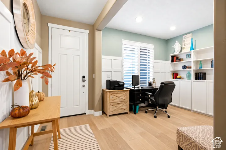Entryway and office space featuring wood-finish flooring, white grid-pattern wainscoting, built-in white cabinetry, and white interior shutters