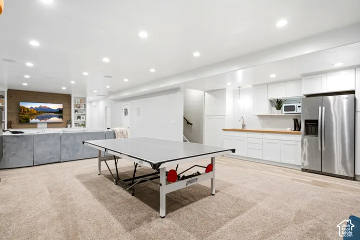 Recessed lighting, wood-finish wall accent, built-in shelving, kitchenette with white cabinetry and butcher block countertop, and stainless steel refrigerator