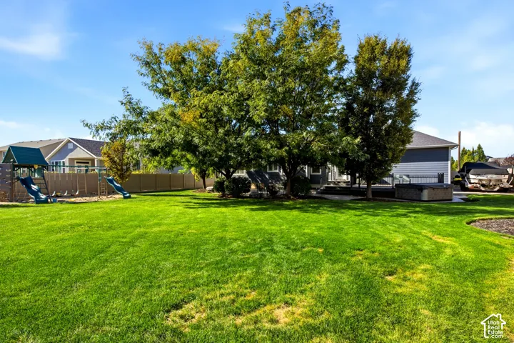 Expansive backyard featuring a large grass lawn, mature trees, perimeter fencing, and a concrete patio