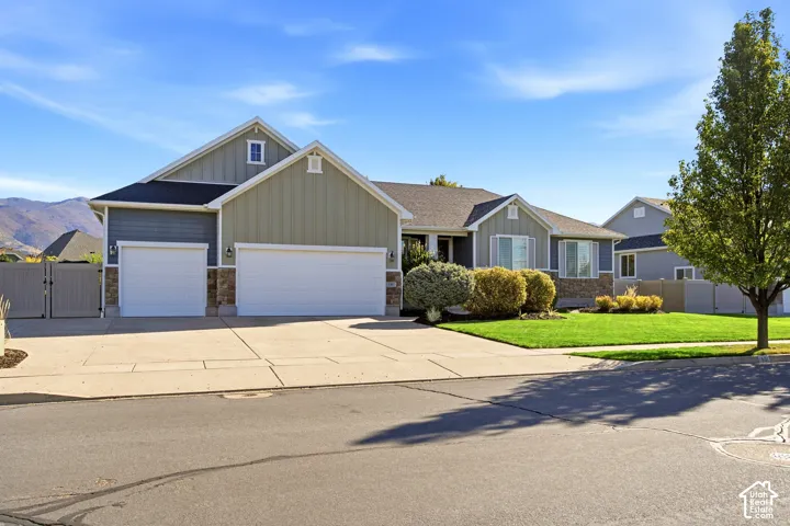 Exterior featuring multi-textured siding, stone veneer accents, an attached three-car garage, and concrete driveway, set against a backdrop of mountain scenery