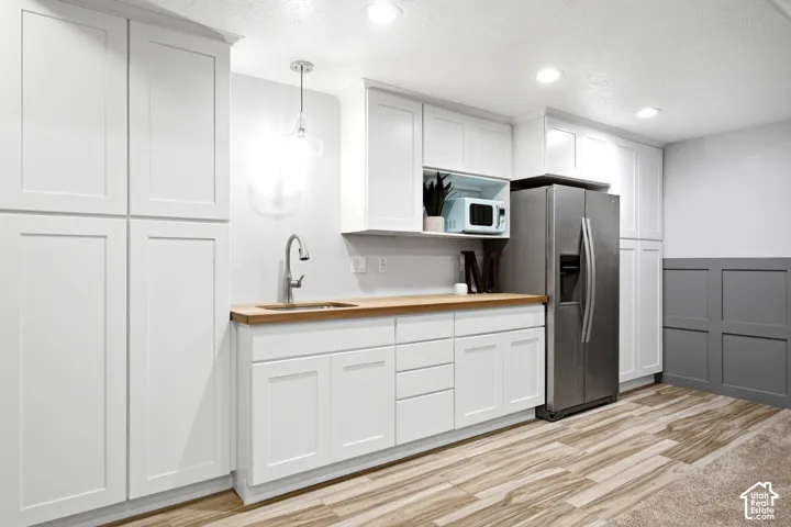 Shaker-style white cabinetry, wood-finish countertops, stainless steel side-by-side refrigerator, under-cabinet sink with high-arc faucet, and charcoal-toned wainscoting
