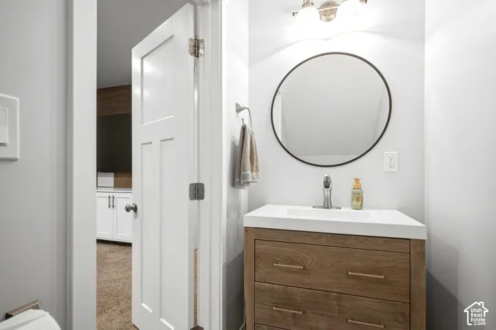 Bathroom featuring a wood-finish vanity with two drawers, a white countertop, an integrated rectangular sink, a circular mirror with a thin frame, and a three-bulb vanity light fixture