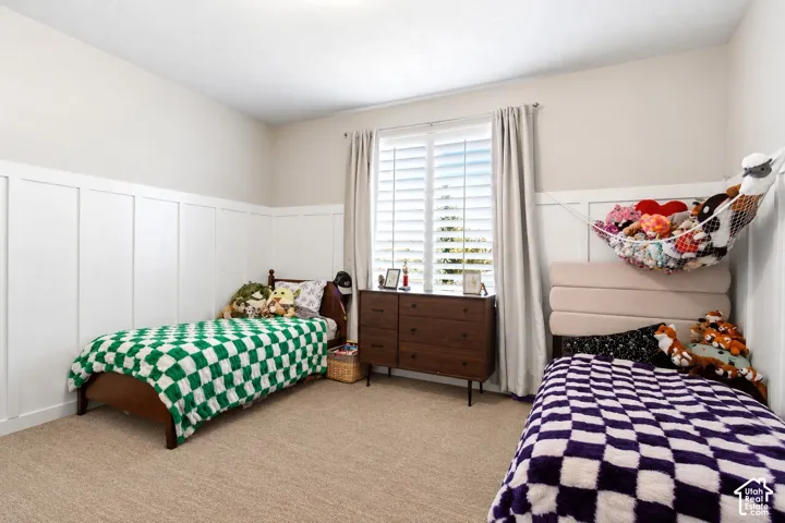 Bedroom featuring white board-and-batten wall paneling, neutral carpeting, and a window fitted with white plantation shutters