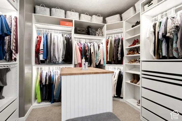 Custom walk-in closet featuring white built-in shelving, a central island with a wood countertop, beadboard paneling, integrated hanging rods, and a stack of pull-out storage drawers