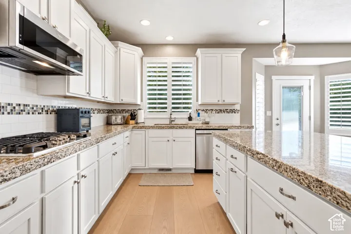 Kitchen featuring white cabinetry, stone countertops, mosaic tile backsplash, wood-finish flooring, and a center island with integrated stainless steel appliances