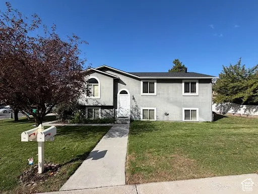 Split-level exterior featuring a stucco facade, arched entryway window, and asphalt shingle roof