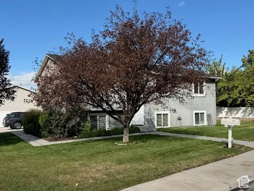 Split-level exterior featuring light-toned stucco siding, a composition shingle roof, concrete walkways, and established landscape elements