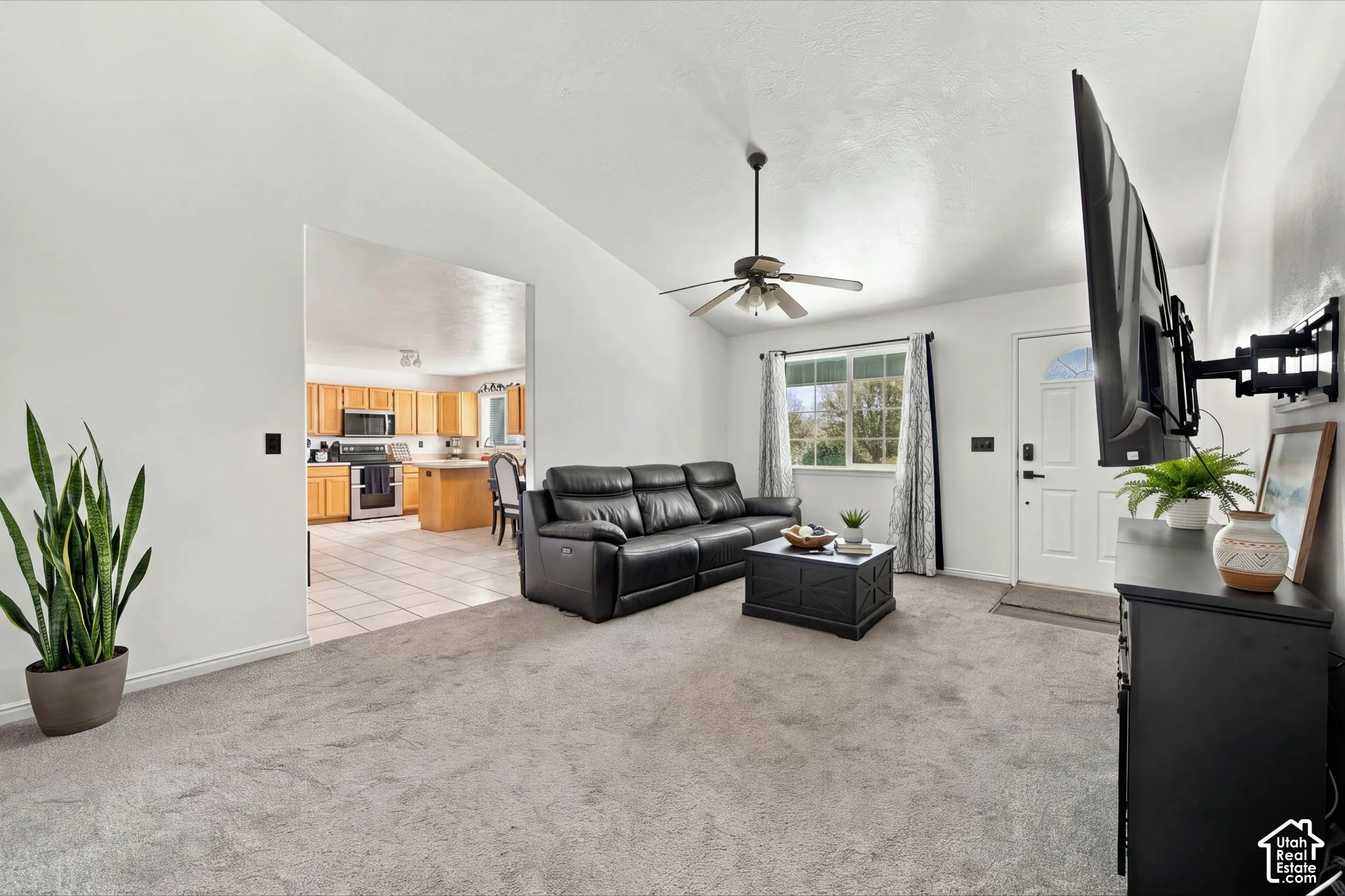 Living area featuring vaulted ceilings, neutral wall tones, carpeted flooring, and a ceiling fan with integrated lighting