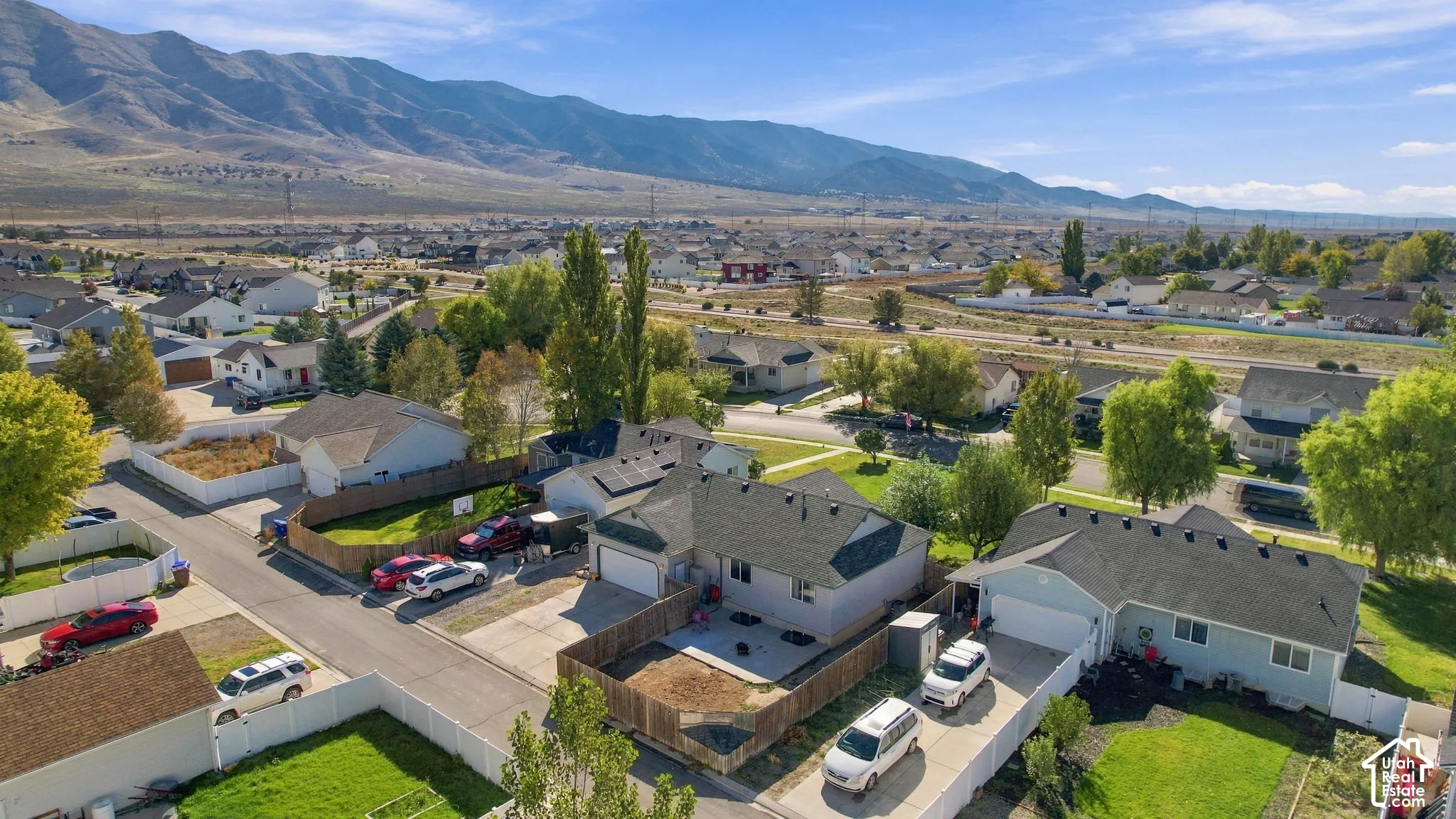Aerial perspective featuring solar panel array, multi-car garages, and fenced yard space against a prominent mountain backdrop
