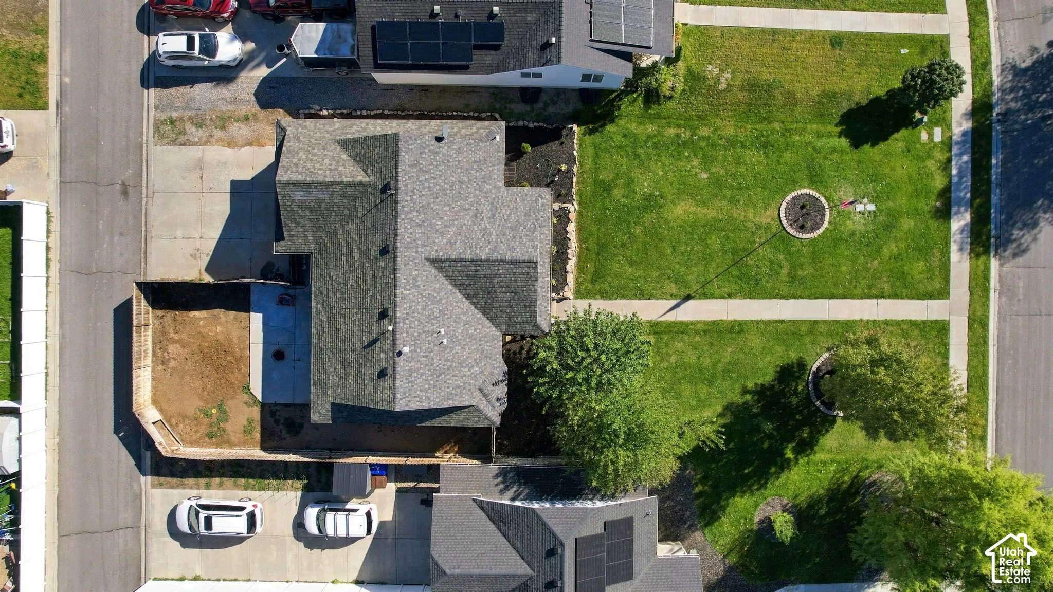 Aerial perspective featuring a multi-gabled asphalt shingle roof, concrete driveway, fenced perimeter, and landscaped grounds with mature trees