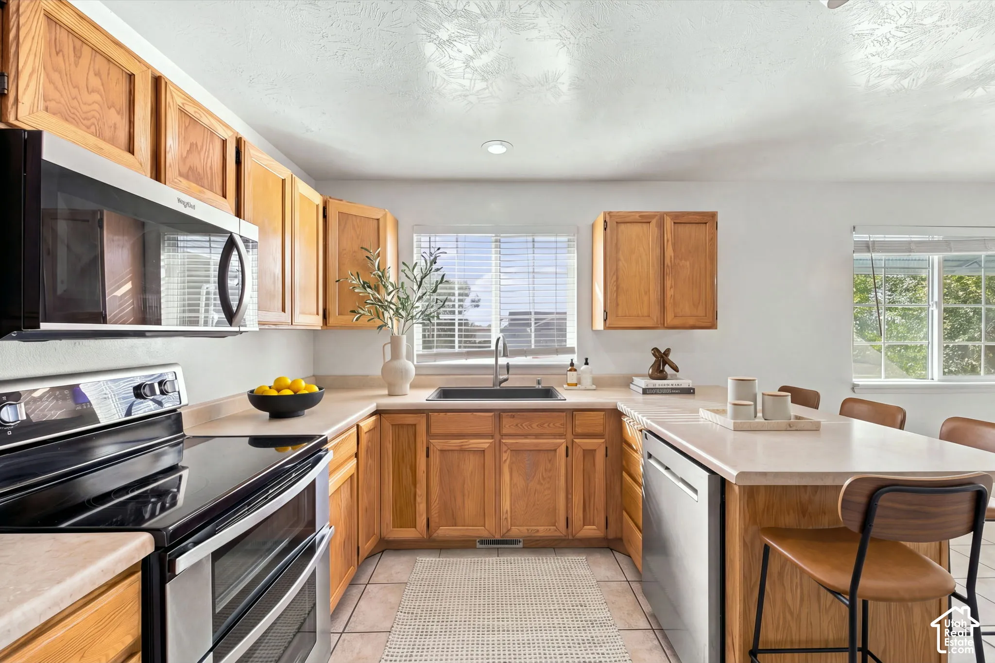 Kitchen featuring natural wood cabinetry, stainless steel appliances, neutral laminate countertops, an undermount sink, and tile flooring