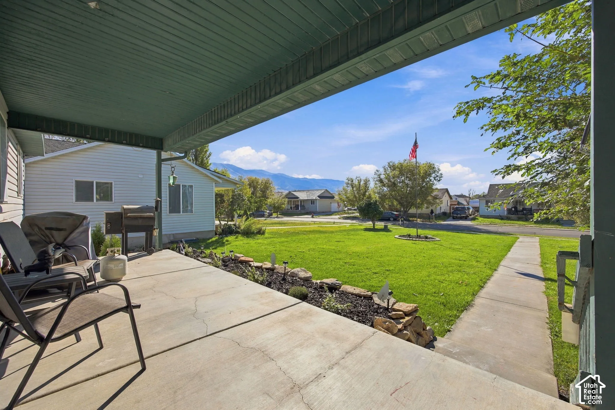 Covered concrete patio featuring a rock-bordered landscaping bed, sprawling lawn, and mountain scenery