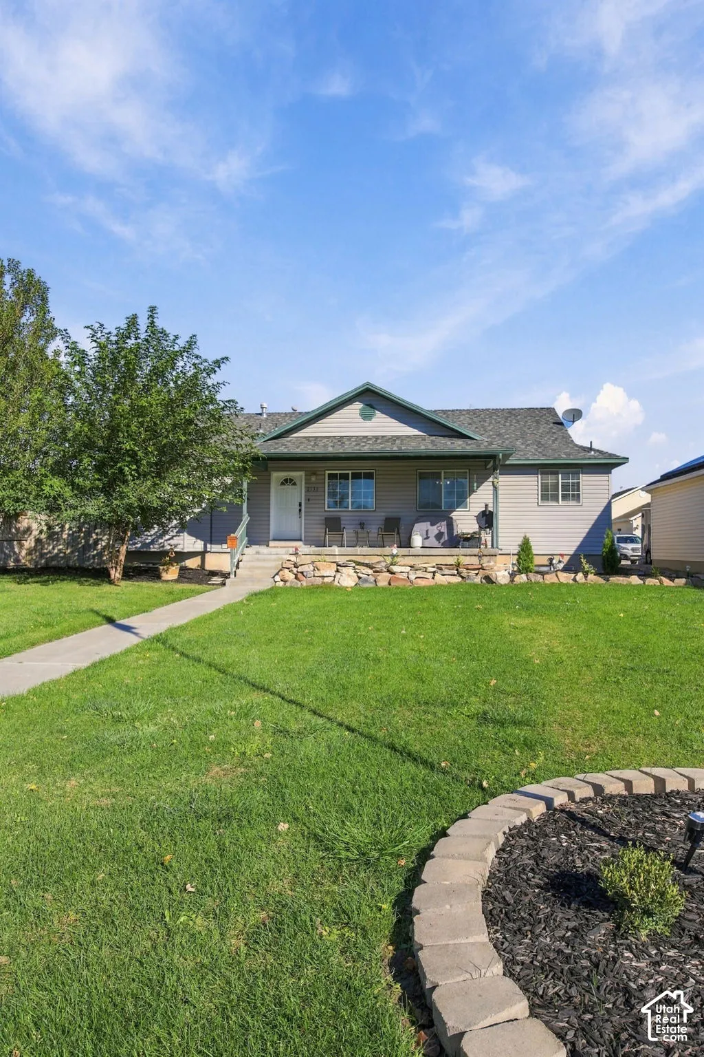 Single-story exterior featuring horizontal siding, a covered front porch, a stone retaining wall, and a concrete walkway