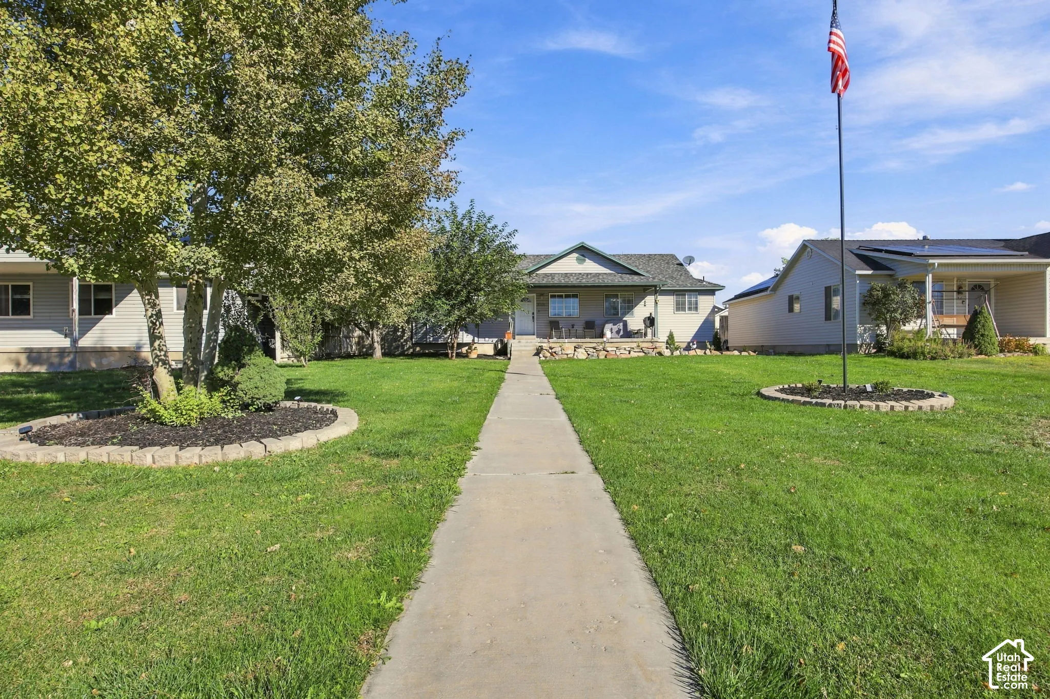 Single-story residence featuring a concrete walkway, stone-accented front porch, low-maintenance siding, mature tree landscaping, and a flag pole