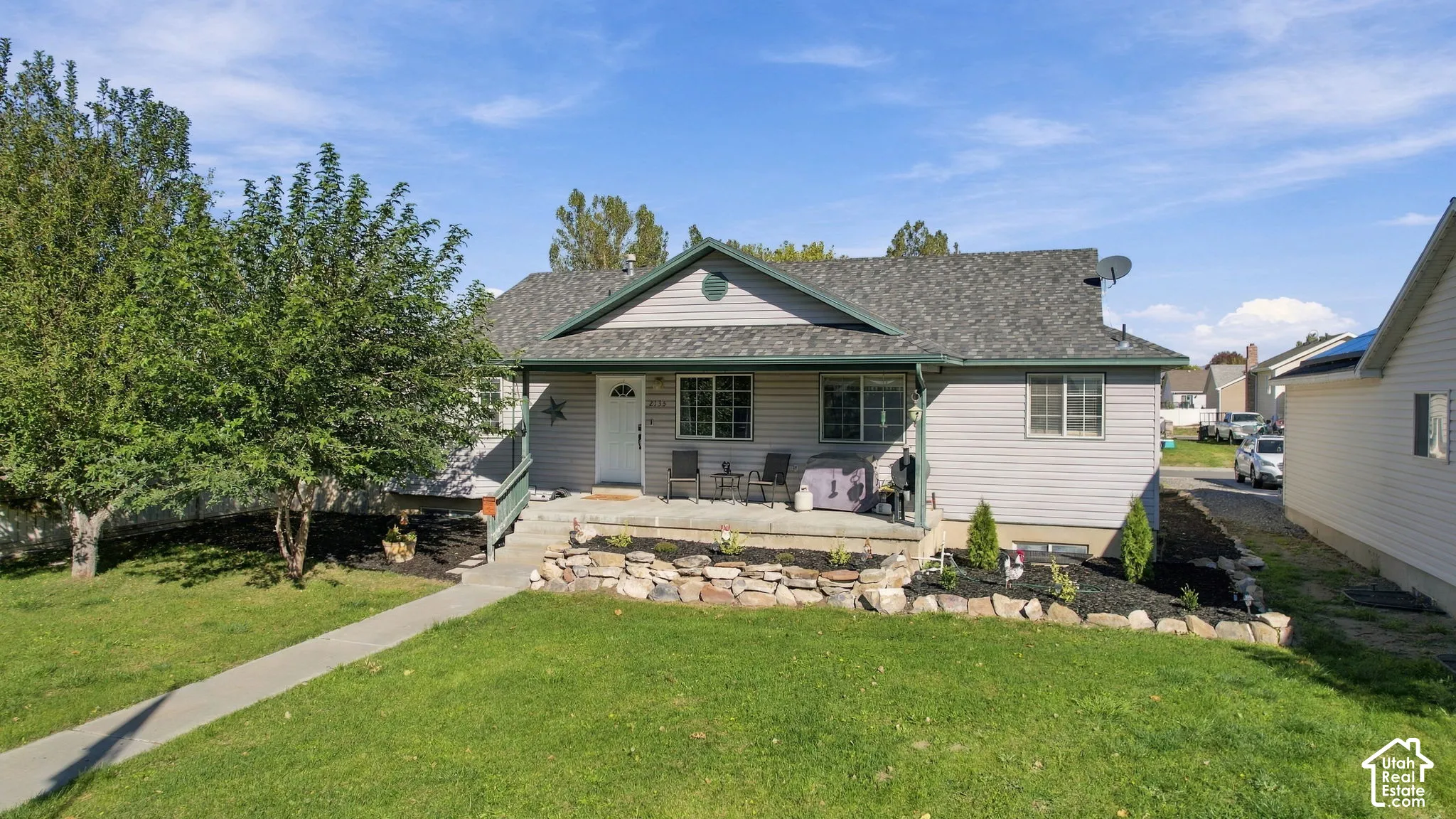 Single-story residence featuring light gray horizontal siding, a covered front porch, an asphalt shingle roof, and a tiered natural stone retaining wall
