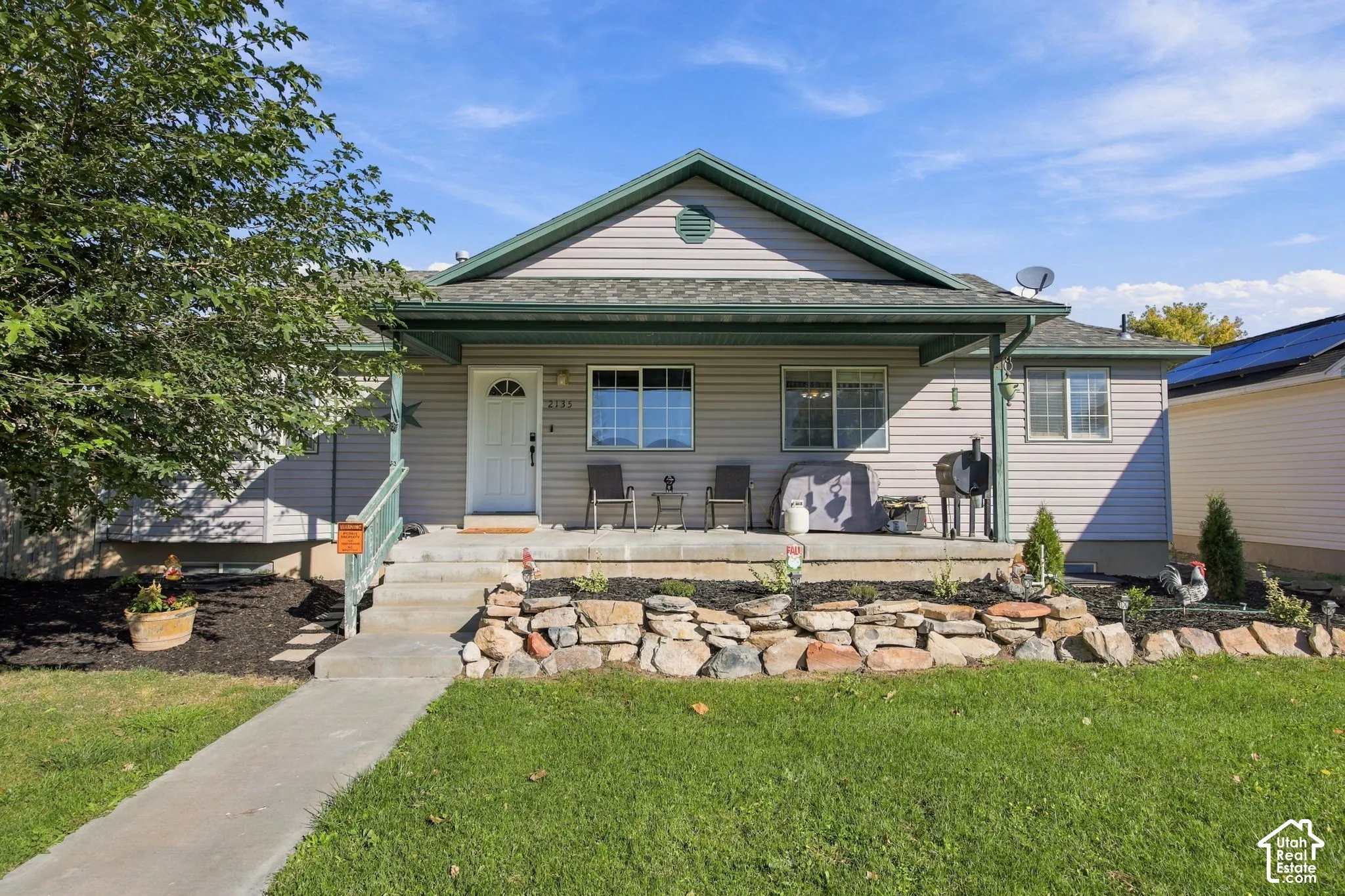 Single-level exterior featuring light-toned horizontal siding, a covered front porch, concrete steps, and a natural stone retaining wall