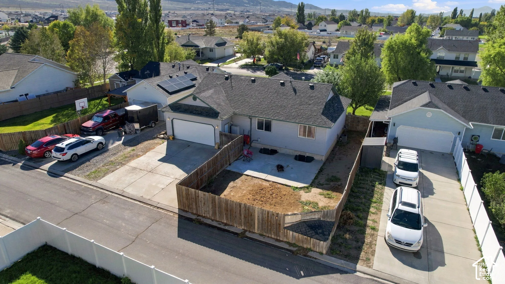 Single-level residence featuring an attached garage, roof-mounted solar panels, a concrete patio, and enclosed wooden fencing