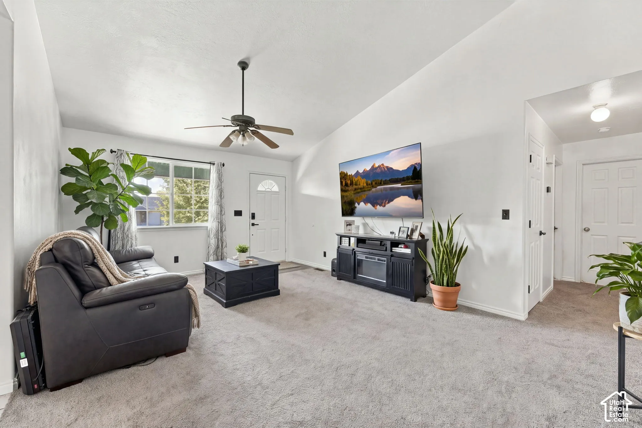 Vaulted ceilings featuring a central paddle fan, wall-to-wall carpeting, and a multi-pane entry door
