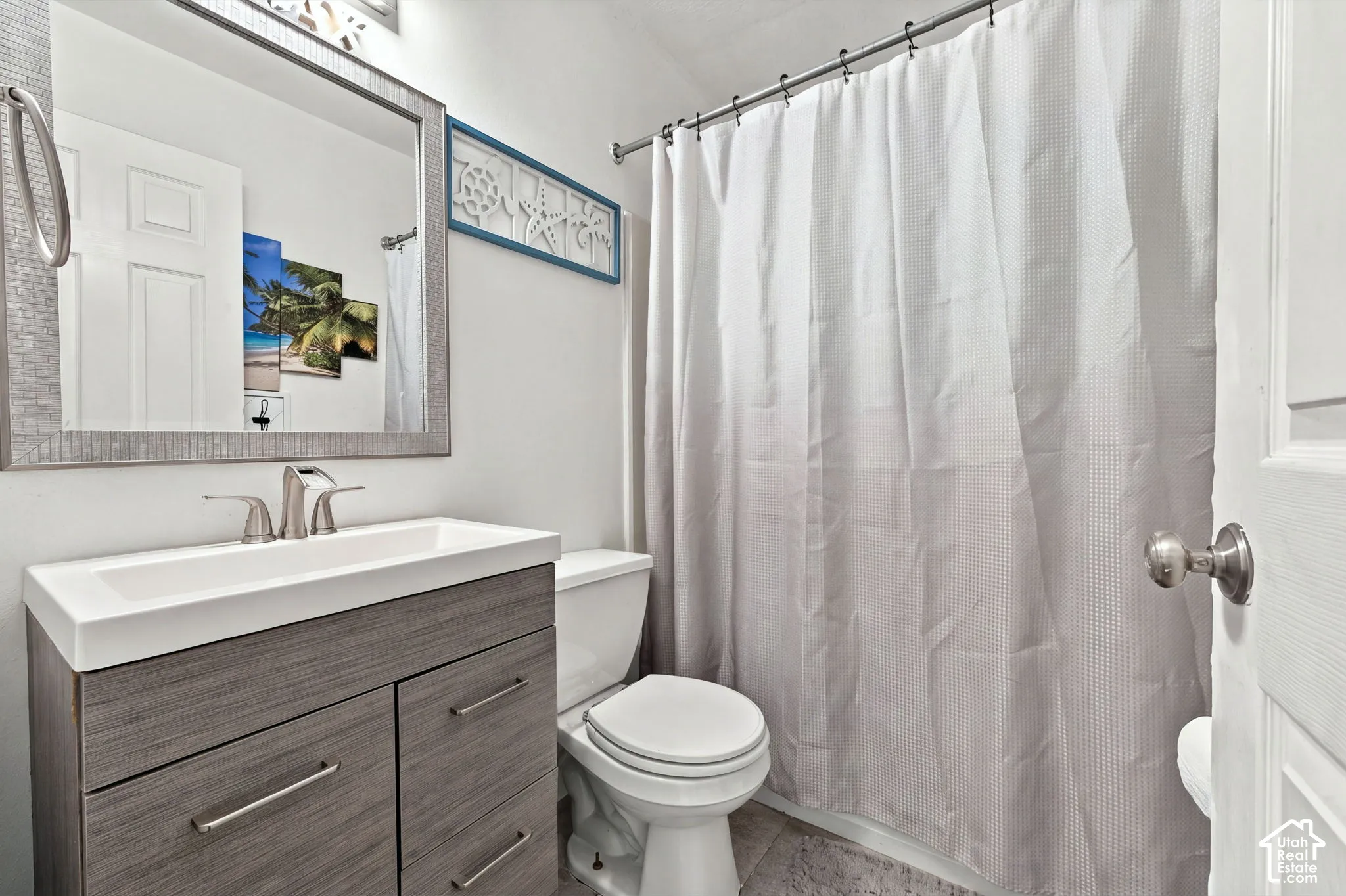 Bathroom featuring a wood-finish vanity with a rectangular sink, brushed nickel faucet, wall-mounted mirror with a textured frame, and a built-in shower rod
