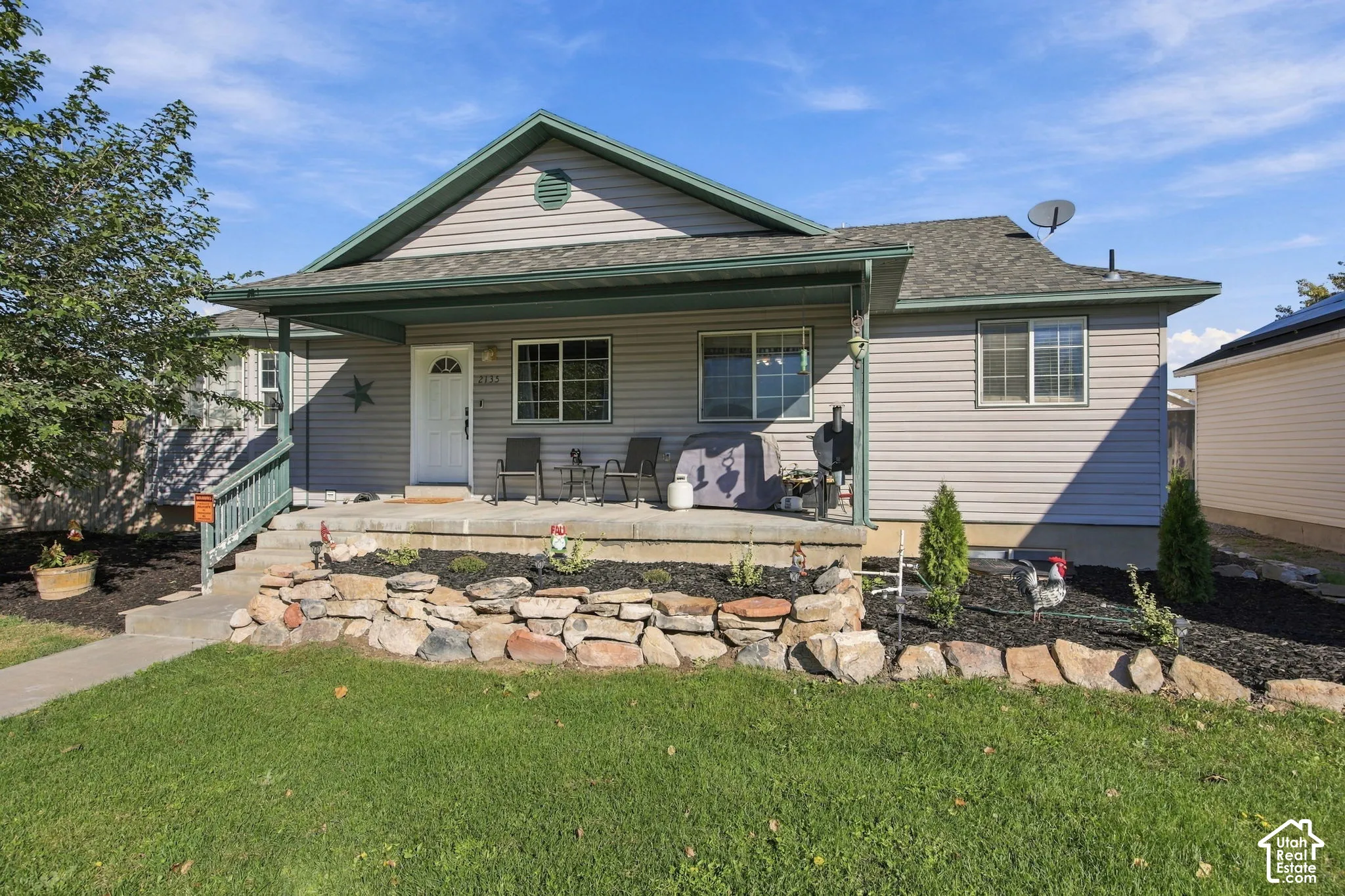 Single-story residence featuring light gray horizontal siding, a covered front porch, and a stacked stone retaining wall