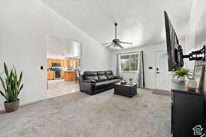 Living area featuring vaulted ceilings, neutral wall tones, carpeted flooring, and a ceiling fan with integrated lighting