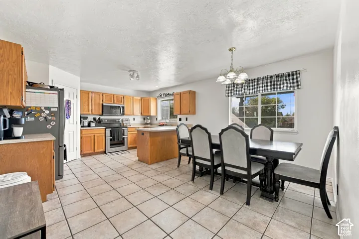Kitchen featuring light wood-finish cabinetry, central island, tile flooring, built-in microwave, and multi-light chandelier