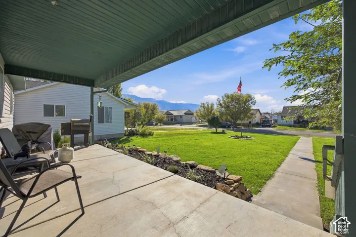Covered concrete patio featuring a rock-bordered landscaping bed, sprawling lawn, and mountain scenery