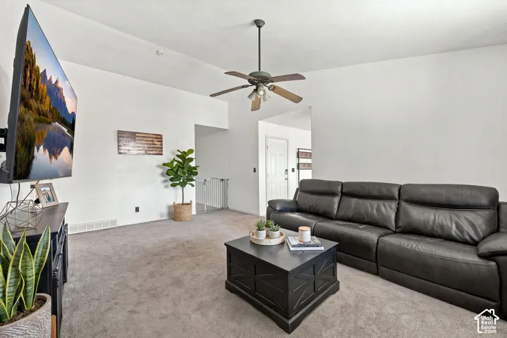 Living area featuring vaulted ceilings, neutral wall-to-wall carpeting, and a ceiling-mounted light fixture with fan