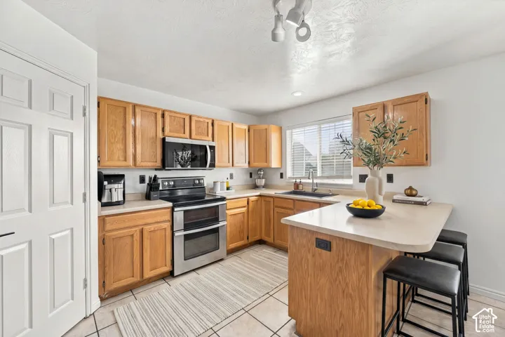 Kitchen featuring oak cabinetry, laminate countertops, stainless steel appliances, ceramic tile flooring, and a peninsula with integrated seating
