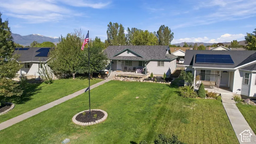 Single-story residence featuring composite shingle roofing, solar panel arrays, stone-accented front porch, flag pole, and mountain backdrop