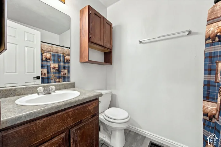 Bathroom featuring a vanity with wood-finish cabinetry, a solid surface countertop, an oval inset sink, wall-mounted storage cabinetry, and wood-finish flooring