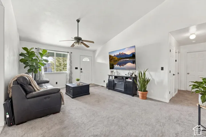Vaulted ceilings featuring a central paddle fan, wall-to-wall carpeting, and a multi-pane entry door