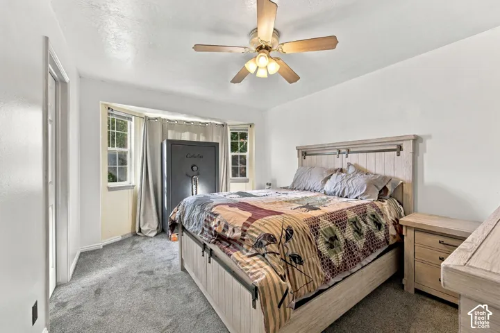 Neutral-toned carpeting, multi-pane bay window, and ceiling-mounted light fixture with a fan