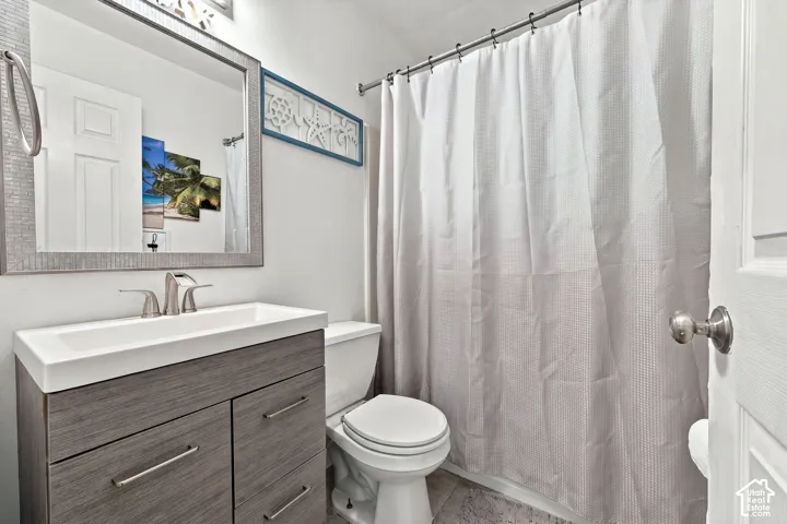 Bathroom featuring a wood-finish vanity with a rectangular sink, brushed nickel faucet, wall-mounted mirror with a textured frame, and a built-in shower rod