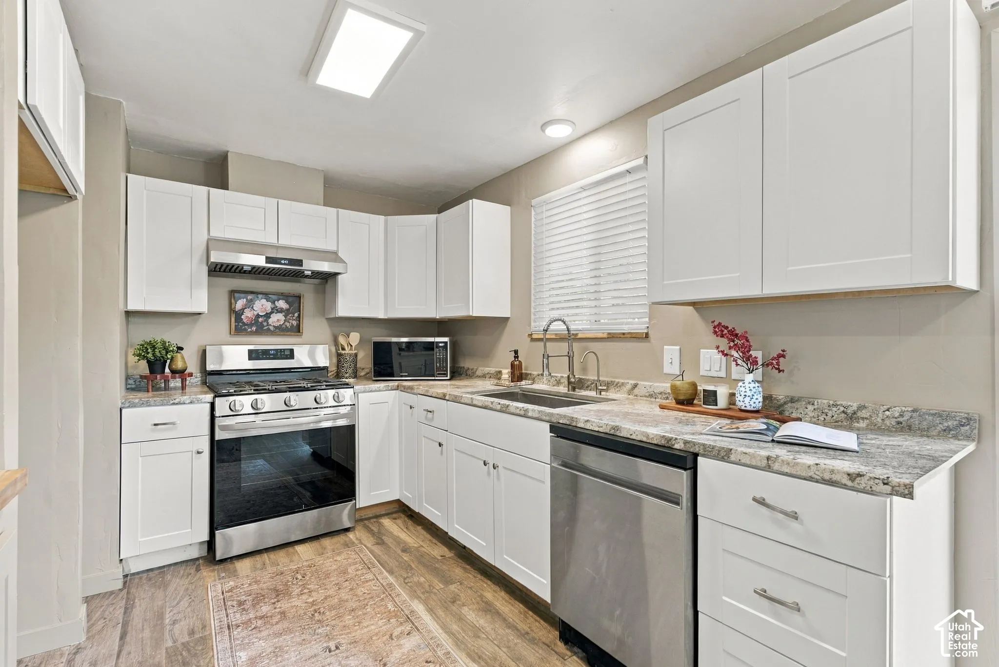 Kitchen featuring white shaker-style cabinetry, stone-patterned laminate countertops, stainless steel appliances, a high-arc kitchen faucet, and wood-finish flooring