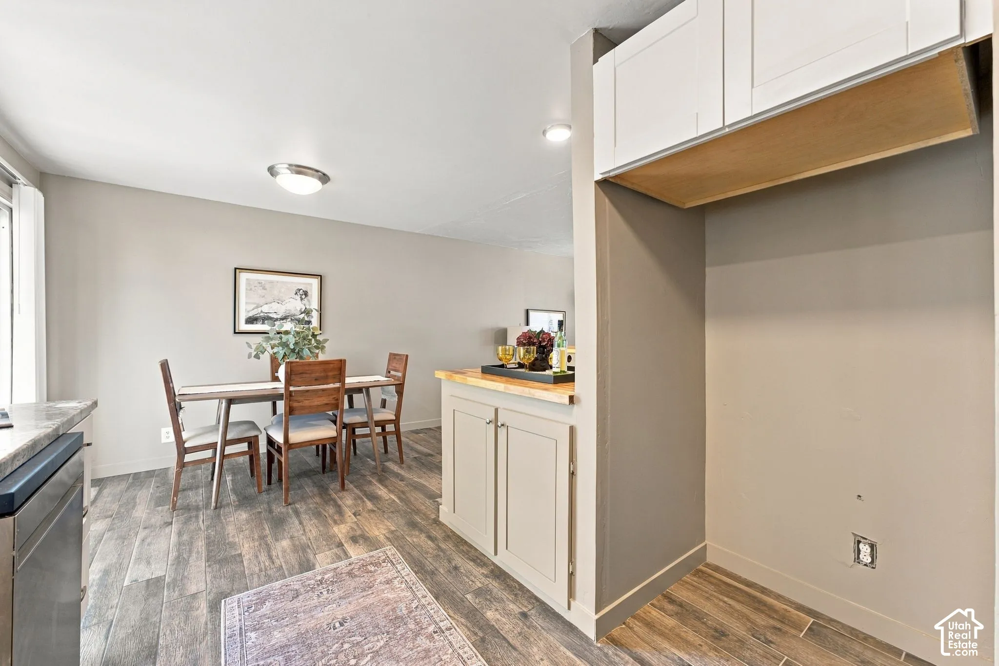 Wood-finish tile flooring, white shaker-style cabinetry, and a natural wood countertop surface