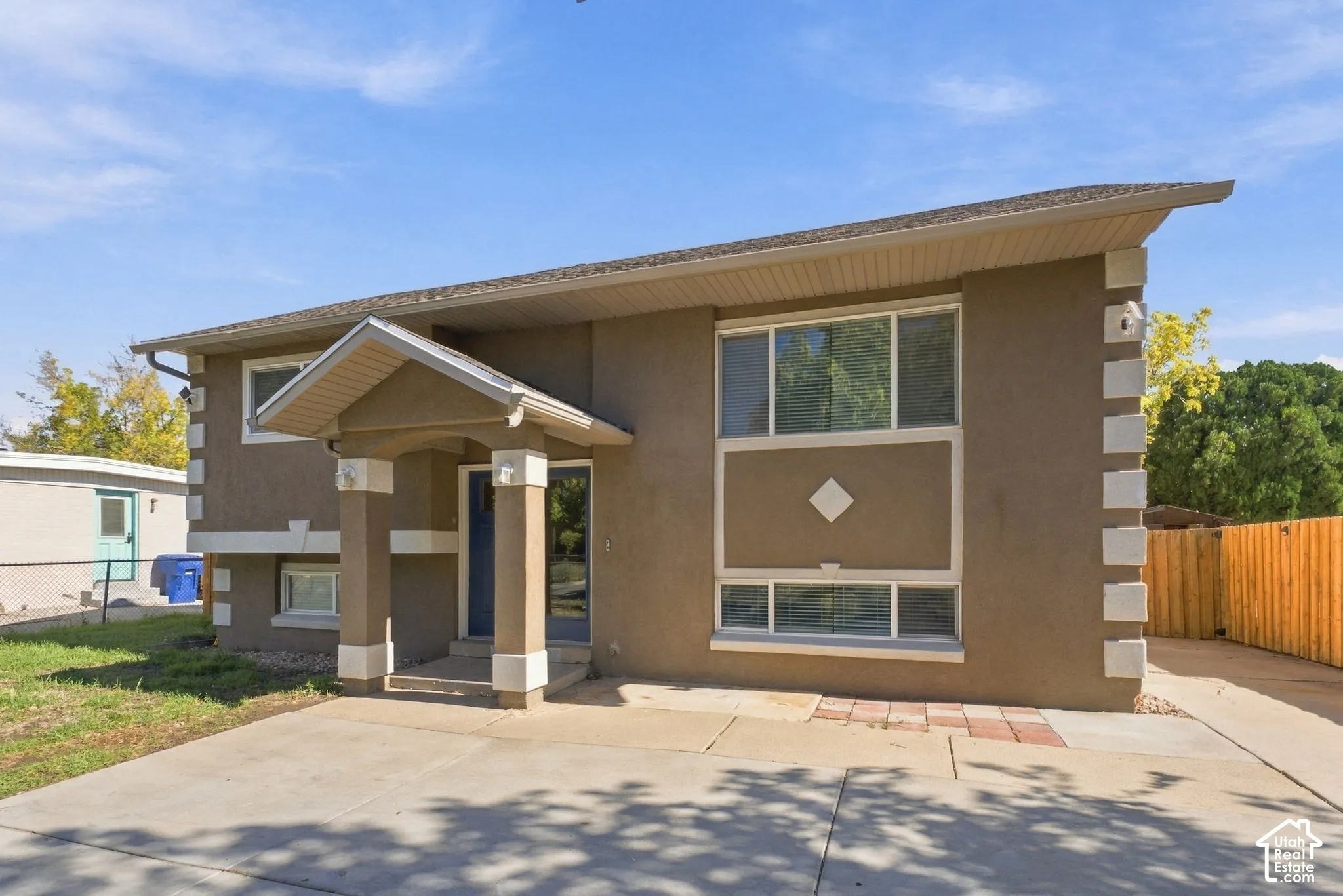 Two-story stucco exterior featuring contrast corner quoins, a covered entryway with structural columns, and a paved concrete driveway